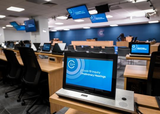Image of Covid Inquiry room with seats and screens with the Covid-19 Inquiry logo on them