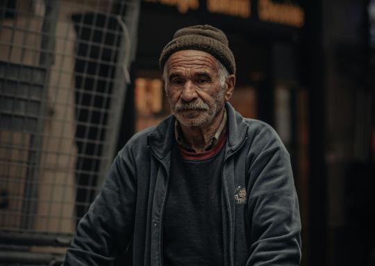 Older man pushing a trolley, wearing a coat and hat